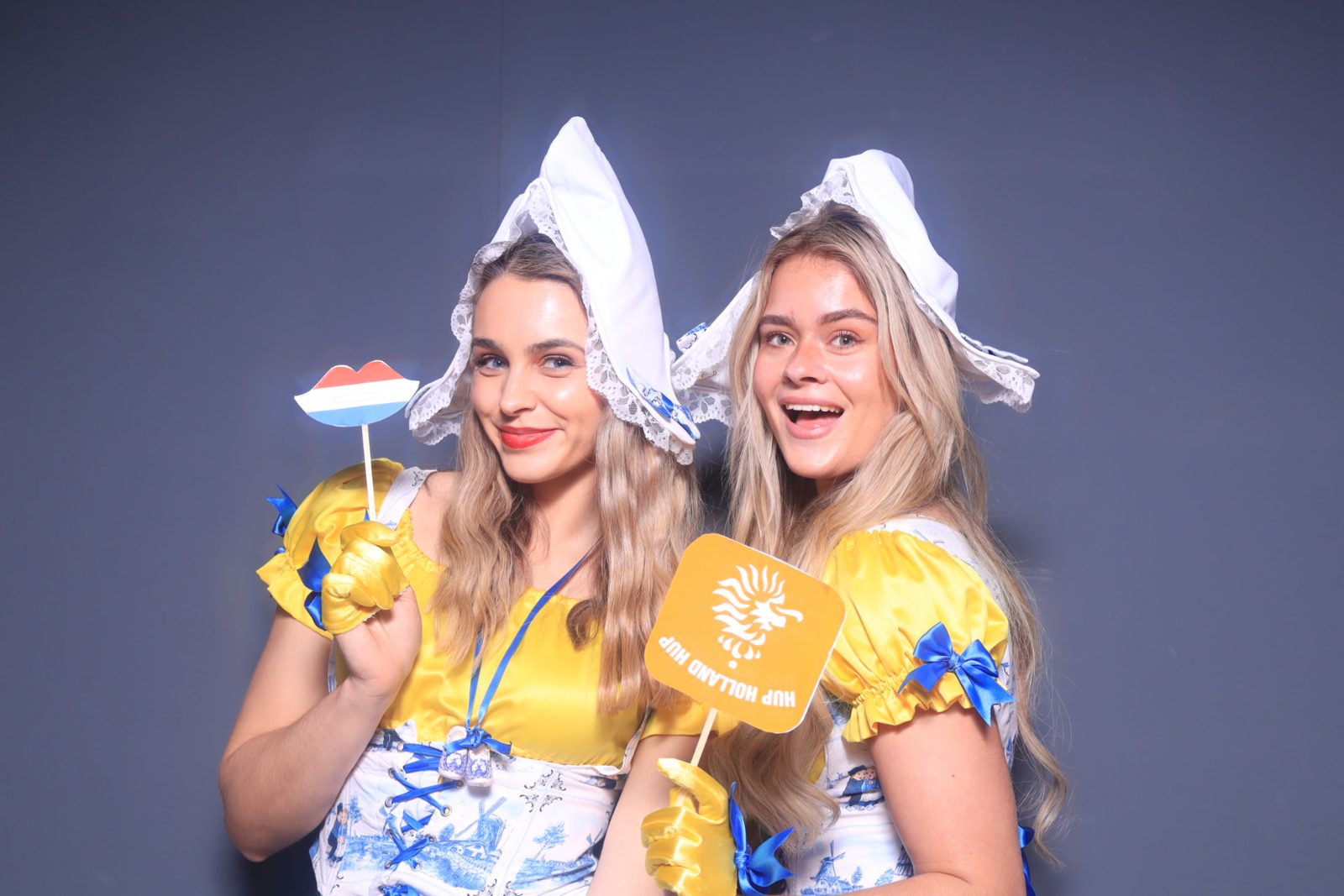 Twee vrouwen in Hollandse klederdracht met oranje rekwisieten, waaronder een bordje met Hup Holland Hup