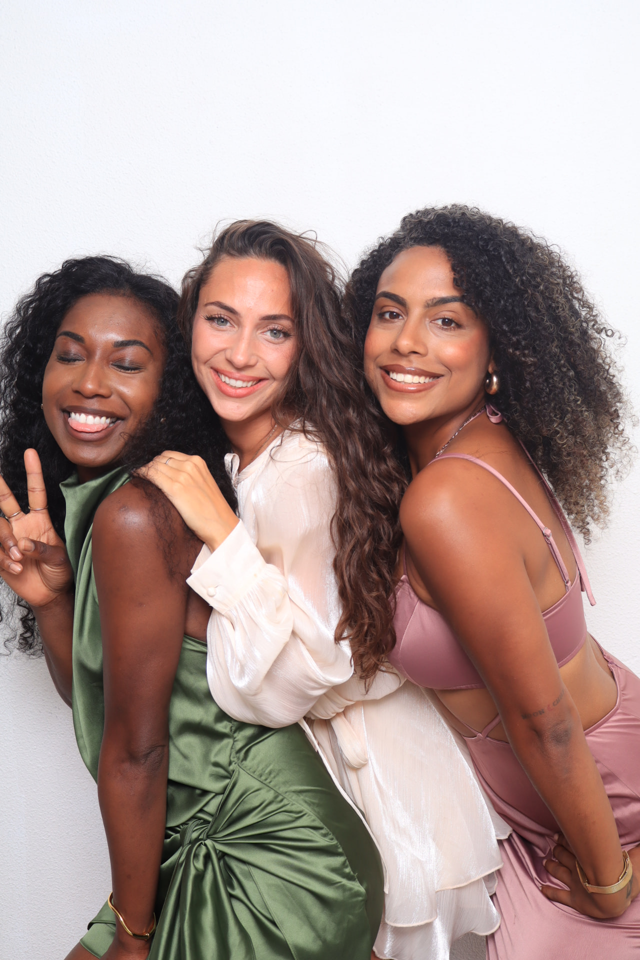 Drie lachende vriendinnen in groene, witte en roze satijnen outfits poseren samen